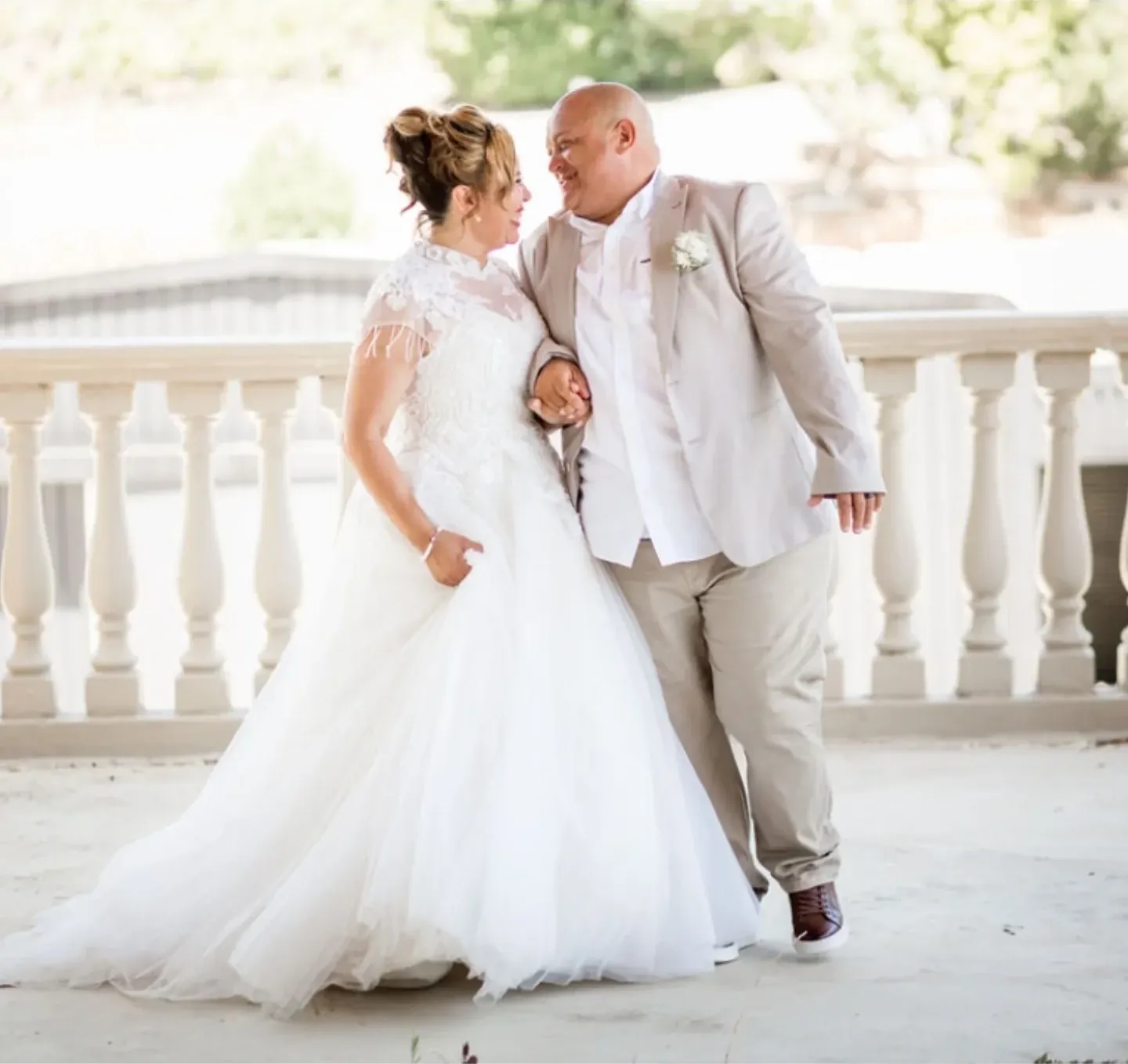 Bride and groom walking arm in arm and smiling at each other beside a white balustrade.